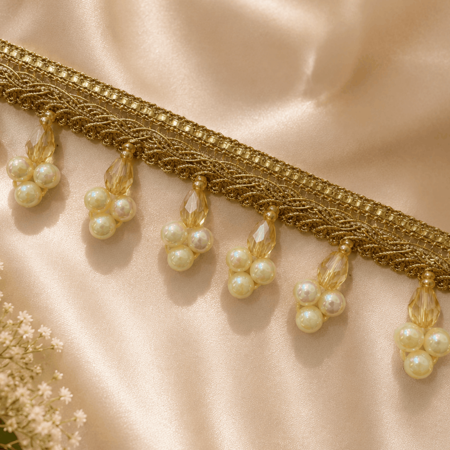Gold lace trim with pearl-like beads on a beige fabric background